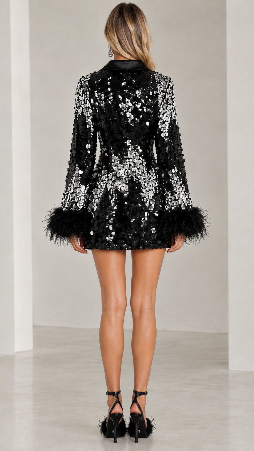 Back view of model wearing black sequin mini dress with long sleeves and feather cuffs