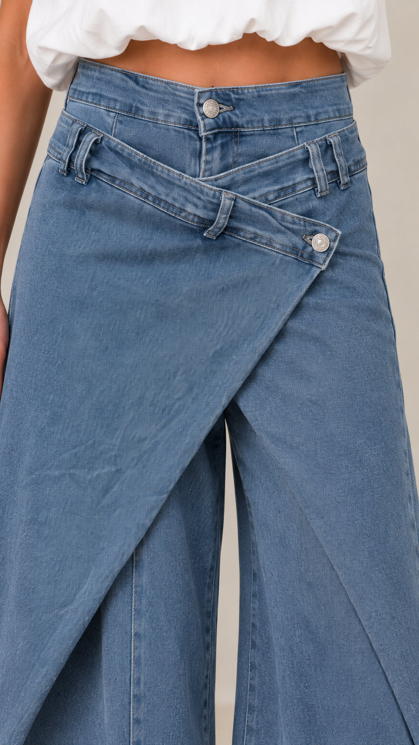 Close-up detail of asymmetrical crossover waistband and button closure on blue denim jeans