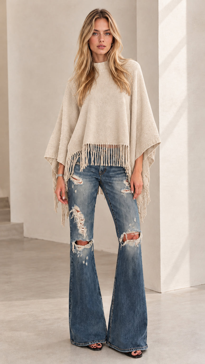 Model wearing beige oatmeal fringe poncho sweater and distressed wide leg jeans